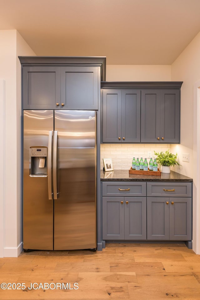 kitchen featuring tasteful backsplash, dark stone countertops, stainless steel fridge, light wood finished floors, and gray cabinetry