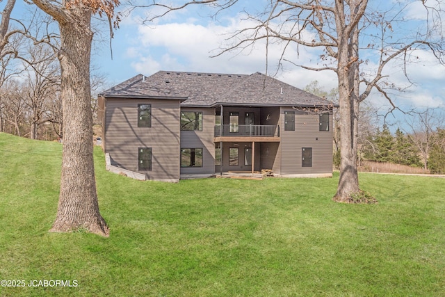 back of property featuring roof with shingles, a balcony, and a lawn