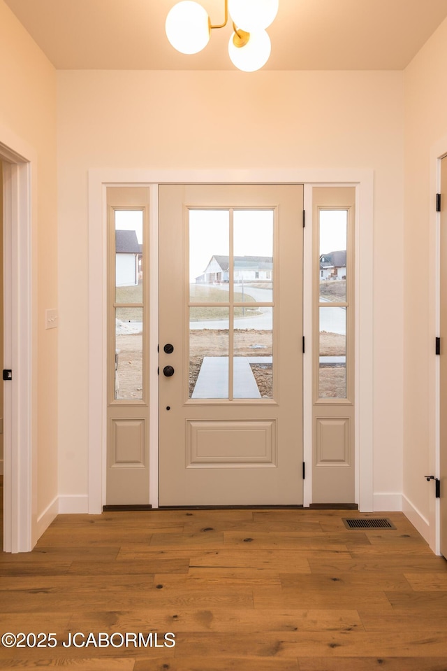 foyer entrance featuring visible vents, baseboards, an inviting chandelier, and wood finished floors