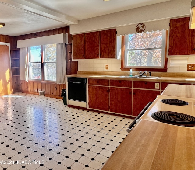 kitchen featuring black dishwasher, tasteful backsplash, wood walls, and sink