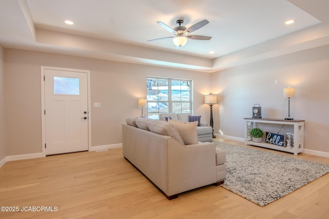 living room with light wood-type flooring, ceiling fan, and a tray ceiling