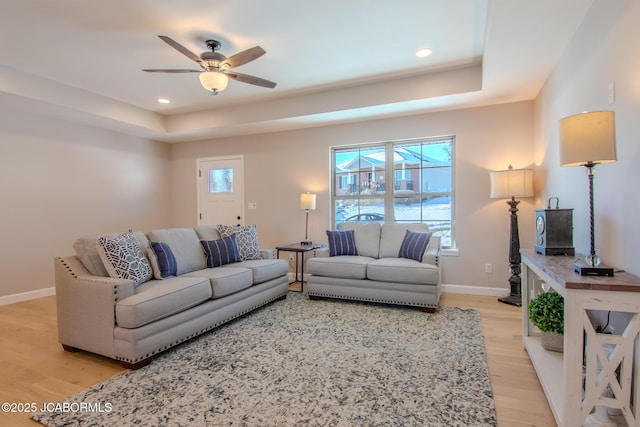 living room with ceiling fan, light wood-type flooring, and a tray ceiling