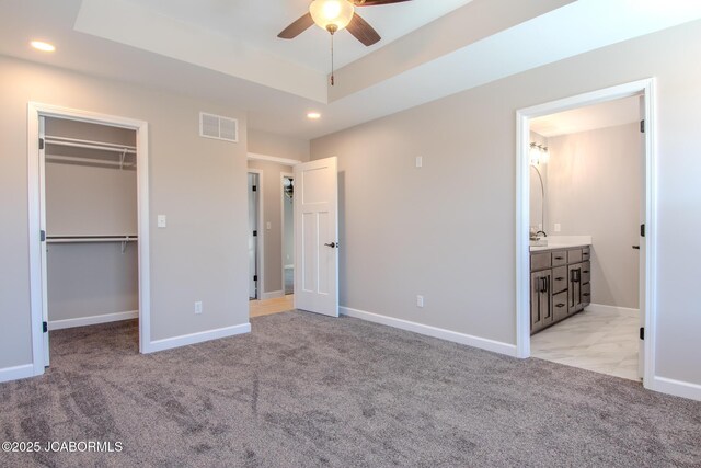 unfurnished bedroom featuring ceiling fan, a tray ceiling, connected bathroom, a walk in closet, and a closet