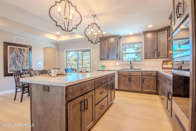 kitchen featuring an inviting chandelier, a center island, decorative light fixtures, light wood-type flooring, and sink