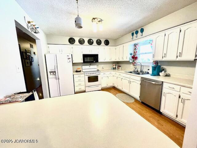 kitchen featuring white appliances, pendant lighting, white cabinets, and sink