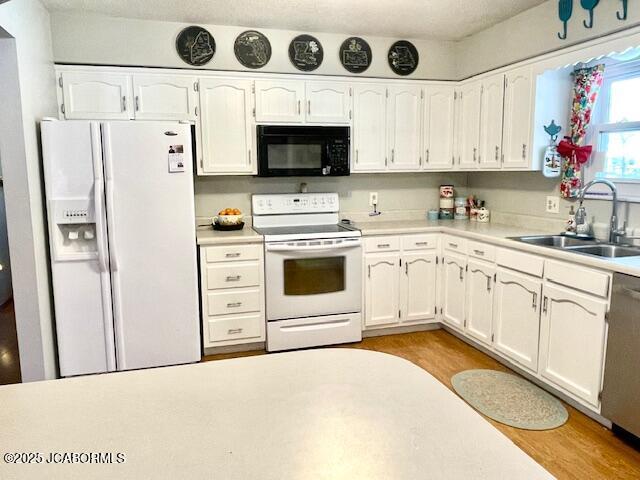 kitchen with white appliances, light wood-type flooring, white cabinets, and sink