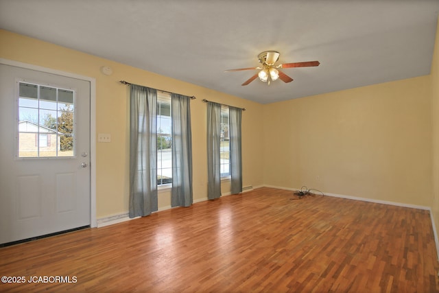 interior space with ceiling fan, wood finished floors, a wealth of natural light, and baseboards