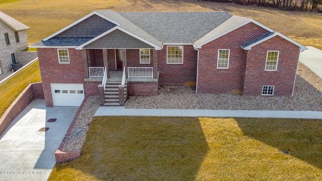 view of front facade featuring brick siding, a porch, a shingled roof, driveway, and a front lawn