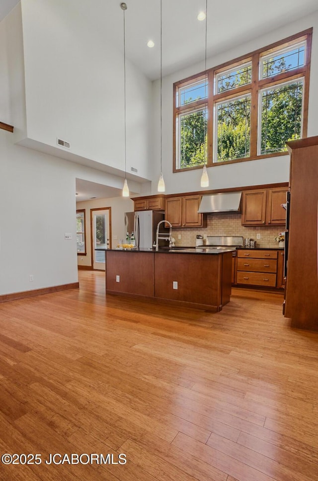 5004 Bates Creek Ct, Columbia, MO 65201 - kitchen with a high ceiling, dark countertops, brown cabinetry, wall chimney range hood, and light wood-style flooring