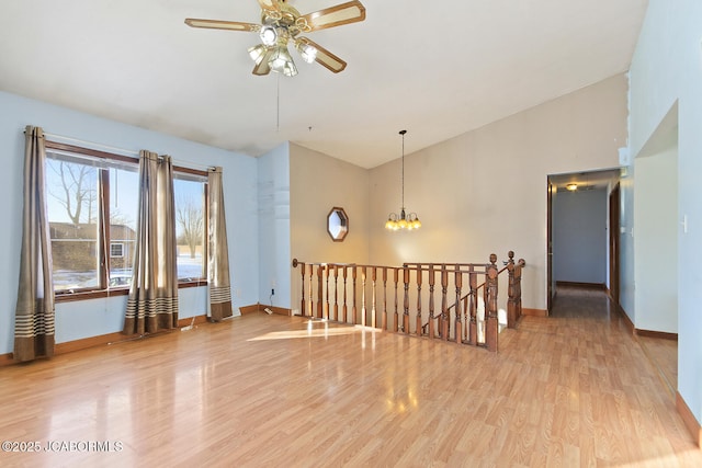 empty room with vaulted ceiling, ceiling fan with notable chandelier, and light wood-type flooring