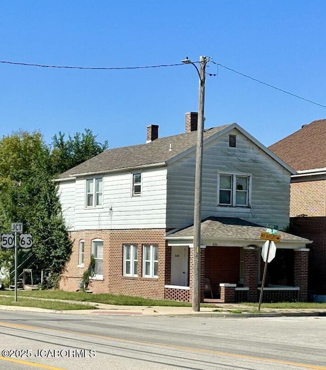 view of front facade with a chimney, brick siding, and covered porch