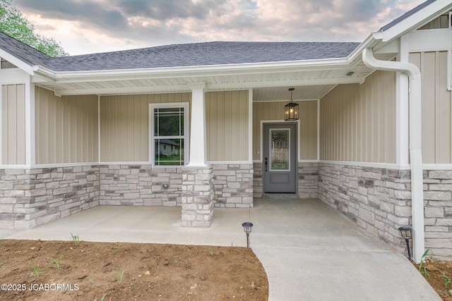 property entrance featuring stone siding, a porch, and a shingled roof