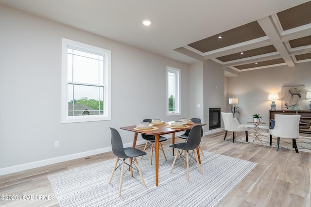 dining room featuring beamed ceiling, baseboards, light wood-style floors, a glass covered fireplace, and coffered ceiling