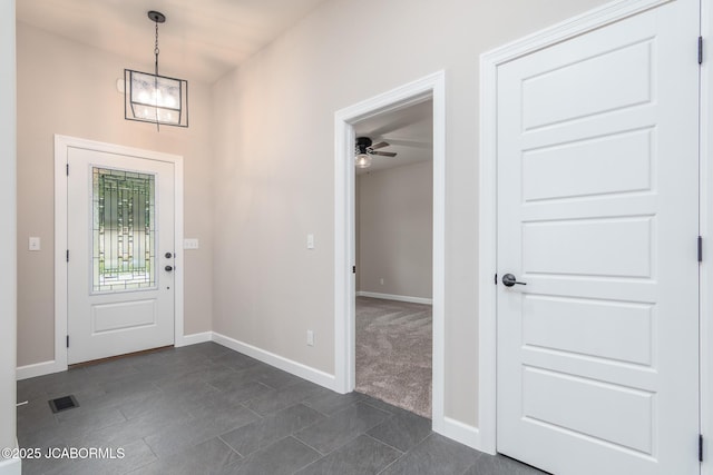 entrance foyer featuring ceiling fan with notable chandelier, visible vents, dark carpet, and baseboards