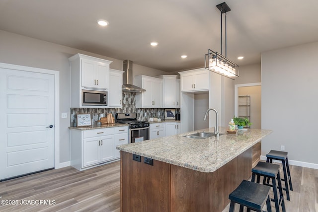 kitchen with light stone counters, a sink, stainless steel appliances, wall chimney range hood, and decorative backsplash