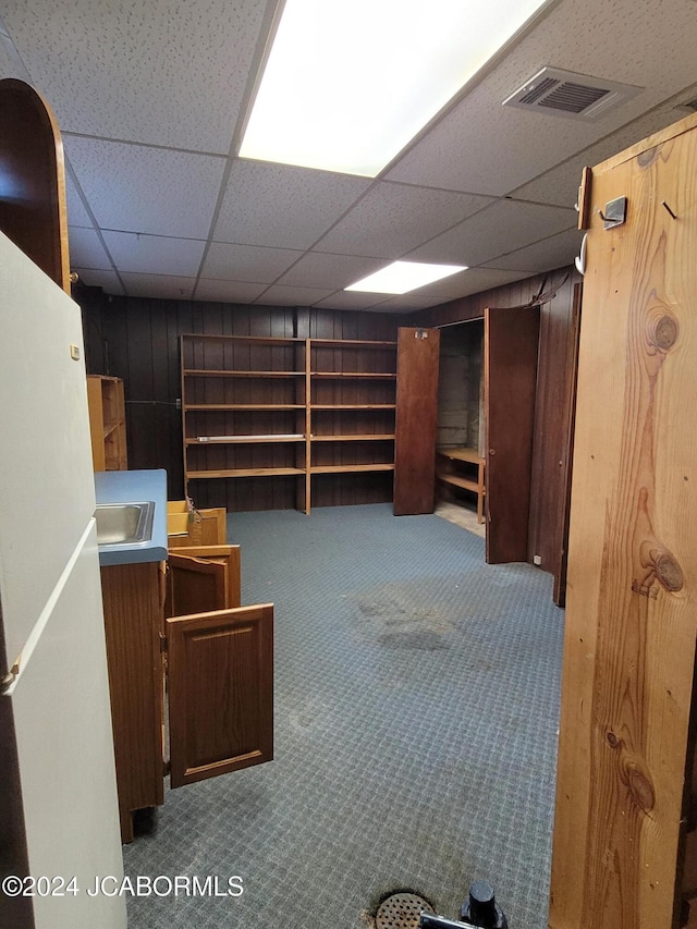 basement with wooden walls, a drop ceiling, and carpet floors