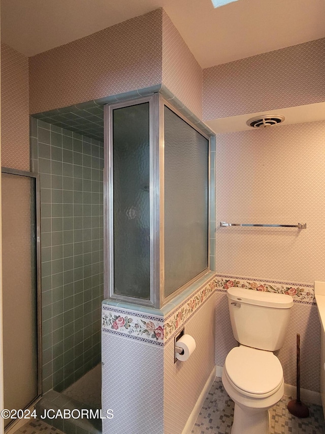 bathroom with tile patterned floors, tiled shower, and toilet