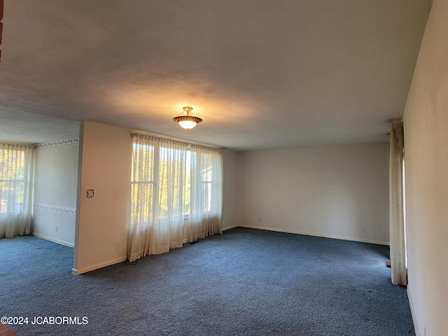 spare room featuring dark colored carpet and a wealth of natural light