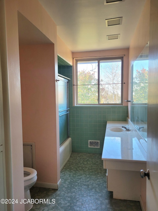 full bathroom featuring vanity, tile patterned floors, toilet, enclosed tub / shower combo, and tile walls