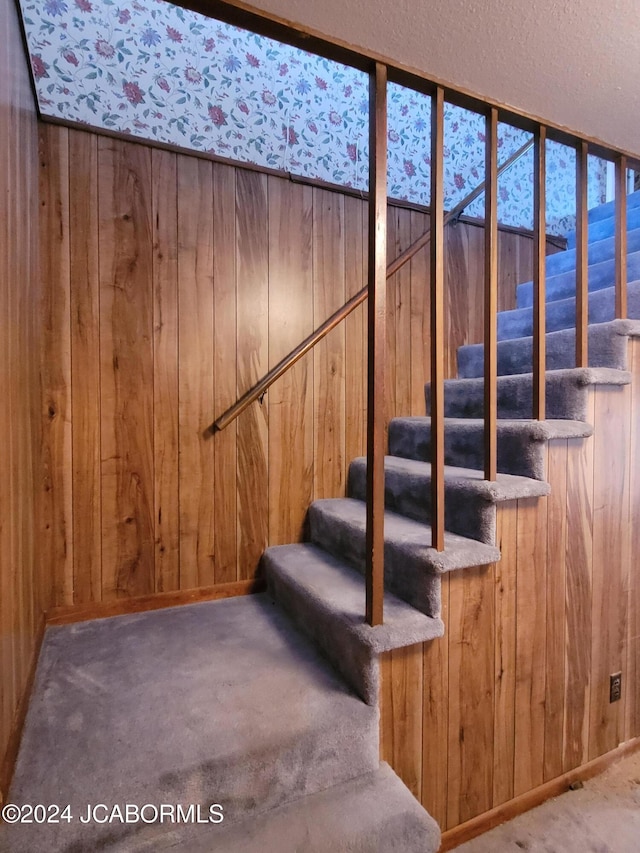 stairs featuring carpet, a textured ceiling, and wooden walls