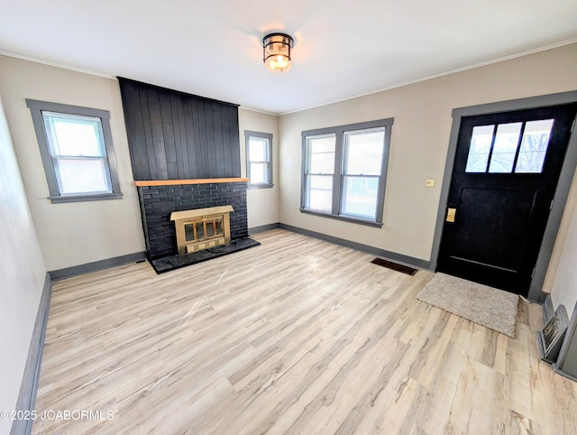 entryway with a brick fireplace, crown molding, and light hardwood / wood-style floors