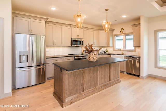 kitchen featuring sink, light hardwood / wood-style flooring, appliances with stainless steel finishes, decorative light fixtures, and a kitchen island