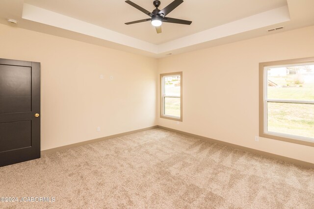 unfurnished room featuring a tray ceiling, light carpet, and ceiling fan