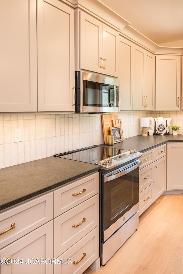 kitchen featuring decorative backsplash, dark stone countertops, light wood-type flooring, and stainless steel appliances