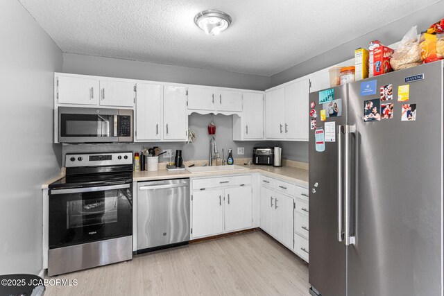 5501 S Brooks Dr, Jefferson City, MO 65109 - kitchen featuring stainless steel appliances, light countertops, light wood finished floors, white cabinets, and a textured ceiling