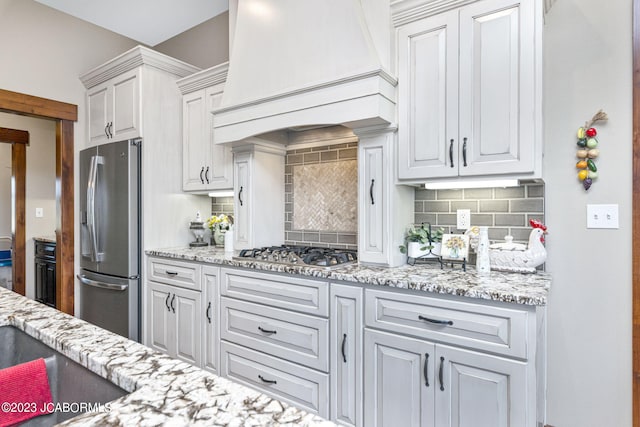 kitchen featuring backsplash, white cabinetry, appliances with stainless steel finishes, light stone countertops, and custom exhaust hood