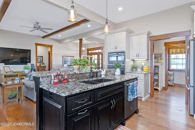 kitchen with a sink, open floor plan, white cabinetry, stainless steel appliances, and dark cabinets