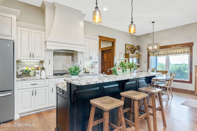 kitchen featuring a kitchen bar, freestanding refrigerator, light wood-style floors, decorative backsplash, and custom exhaust hood