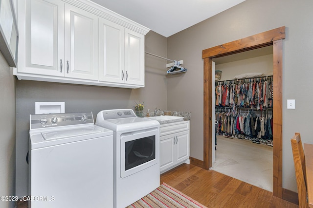 laundry room with cabinet space, light wood-style flooring, washing machine and dryer, and a sink