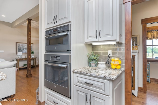 kitchen with decorative backsplash, double oven, light wood-style floors, and white cabinetry