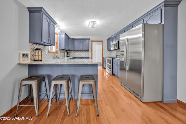 990 Diamond Rdg, Jefferson City, MO 65109 - kitchen featuring a textured ceiling, a sink, a peninsula, light wood-style floors, and stainless steel appliances
