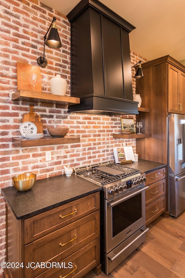 kitchen with premium range hood, brick wall, dark brown cabinets, stainless steel appliances, and light hardwood / wood-style flooring