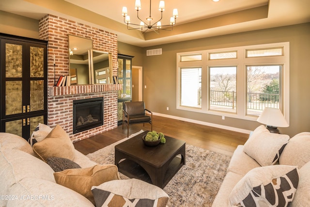 living room featuring a raised ceiling, a fireplace, wood-type flooring, and an inviting chandelier