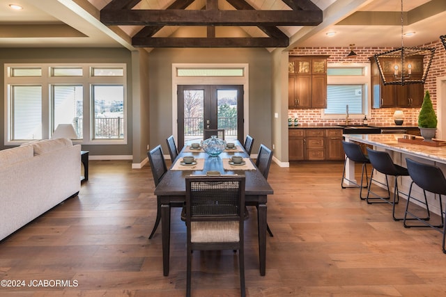 dining space featuring french doors, lofted ceiling with beams, a notable chandelier, and wood-type flooring