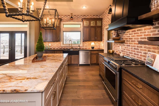 kitchen featuring appliances with stainless steel finishes, light stone counters, wall chimney exhaust hood, brick wall, and sink