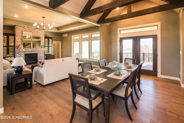 dining room with french doors, a brick fireplace, dark wood-type flooring, an inviting chandelier, and beamed ceiling