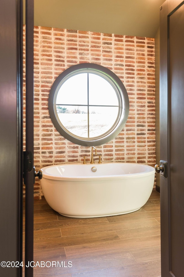 bathroom featuring a washtub, brick wall, and hardwood / wood-style flooring