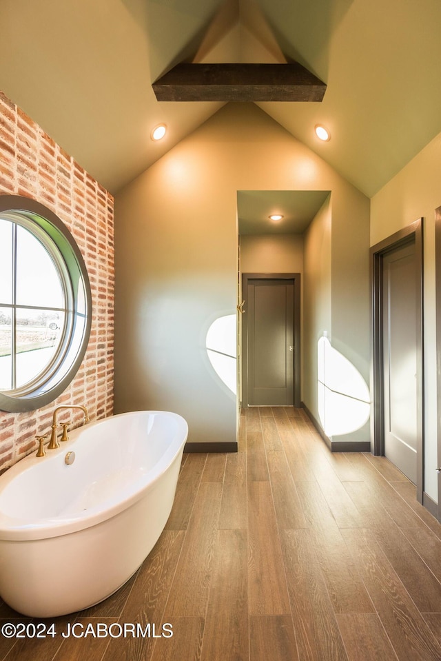 bathroom featuring wood-type flooring, vaulted ceiling with beams, and a bathtub