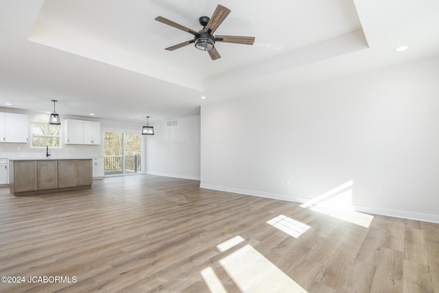 unfurnished living room featuring ceiling fan, light hardwood / wood-style flooring, and a tray ceiling