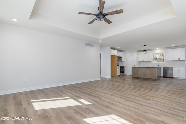 unfurnished living room featuring a raised ceiling, ceiling fan, sink, and light hardwood / wood-style floors