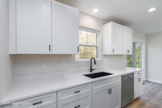 kitchen featuring light stone countertops, stainless steel dishwasher, sink, wood-type flooring, and white cabinetry