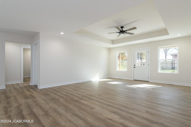 unfurnished living room featuring a raised ceiling, ceiling fan, and wood-type flooring