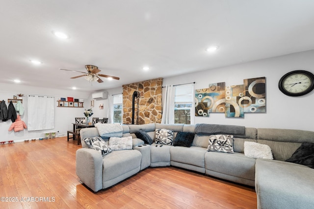 living room featuring ceiling fan, wood-type flooring, a wall mounted air conditioner, and a wood stove