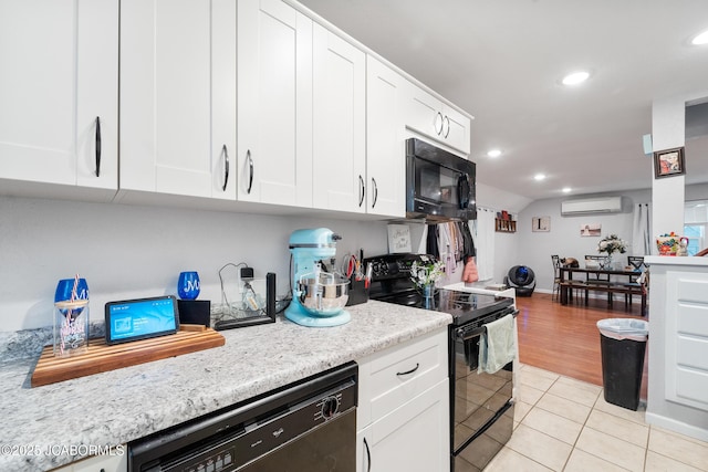 kitchen featuring white cabinetry, a wall mounted AC, light tile patterned floors, black appliances, and light stone countertops