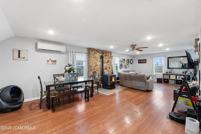 living room featuring plenty of natural light, a wall mounted AC, light hardwood / wood-style flooring, and a wood stove