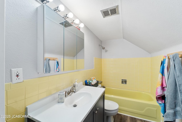 bathroom featuring a tub to relax in, lofted ceiling, a textured ceiling, tile walls, and vanity